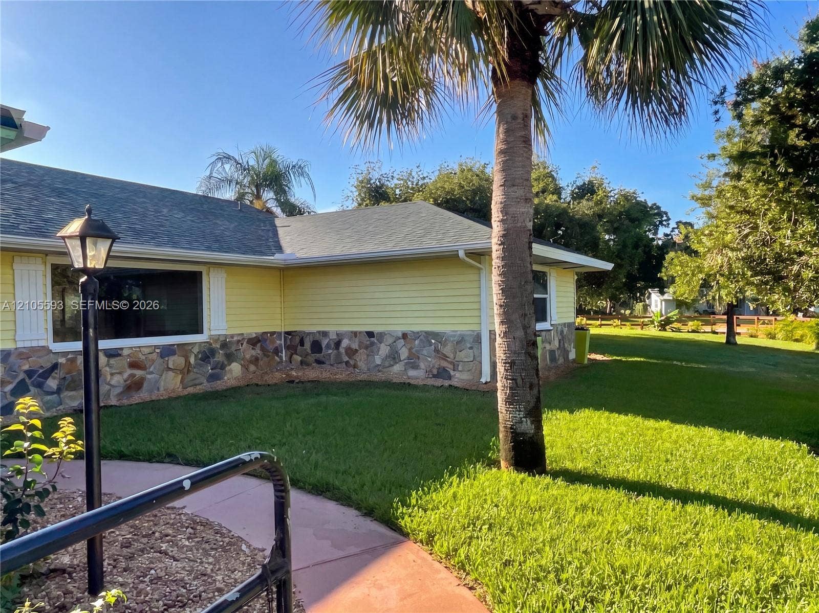 597 Grace Street, Sebastian, FL 32958 Exterior featuring light-colored horizontal siding, natural stone wainscoting, a shingled roof, a curved concrete walkway, and a mature palm tree