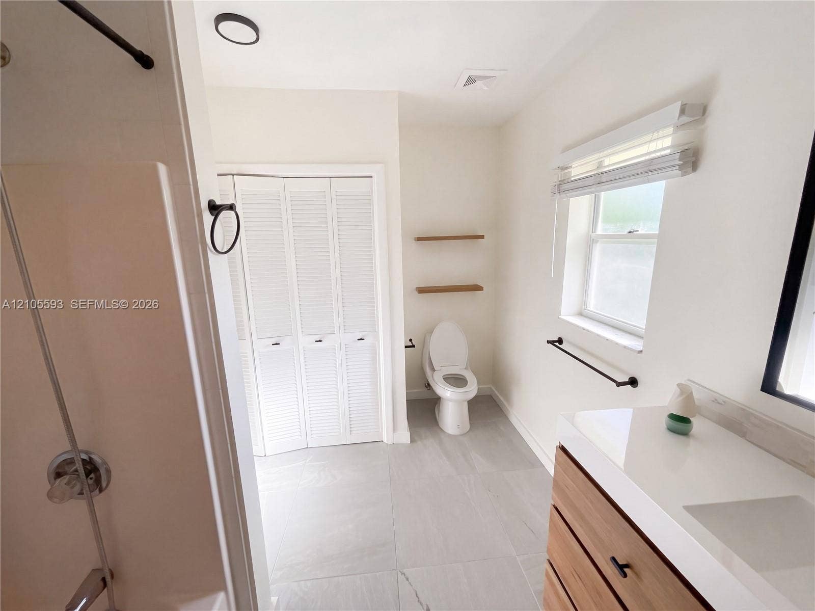 597 Grace Street, Sebastian, FL 32958 Bathroom featuring a vanity with a white countertop, wood-finish cabinetry, matte black hardware, large-format tile flooring, and a bifold closet
