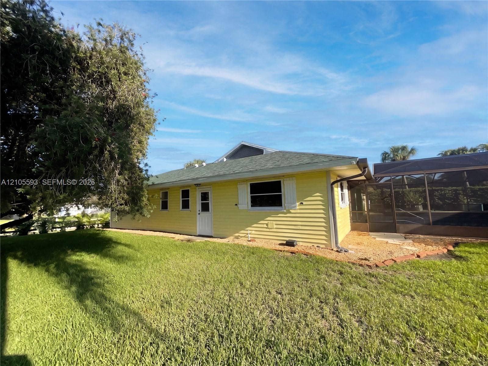 597 Grace Street, Sebastian, FL 32958 Exterior featuring yellow siding, shutter-accented windows, a shingled roof, and an enclosed screened-in area