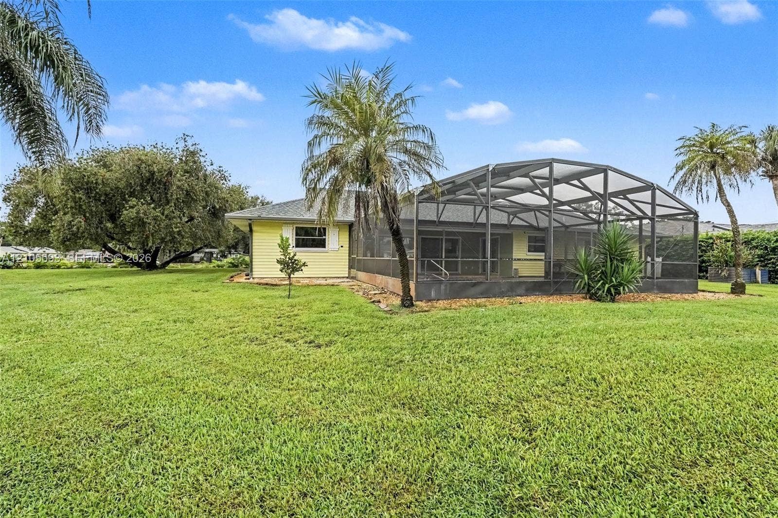 597 Grace Street, Sebastian, FL 32958 Exterior siding, screen-enclosed patio, and expansive lawn featuring mature trees and palms