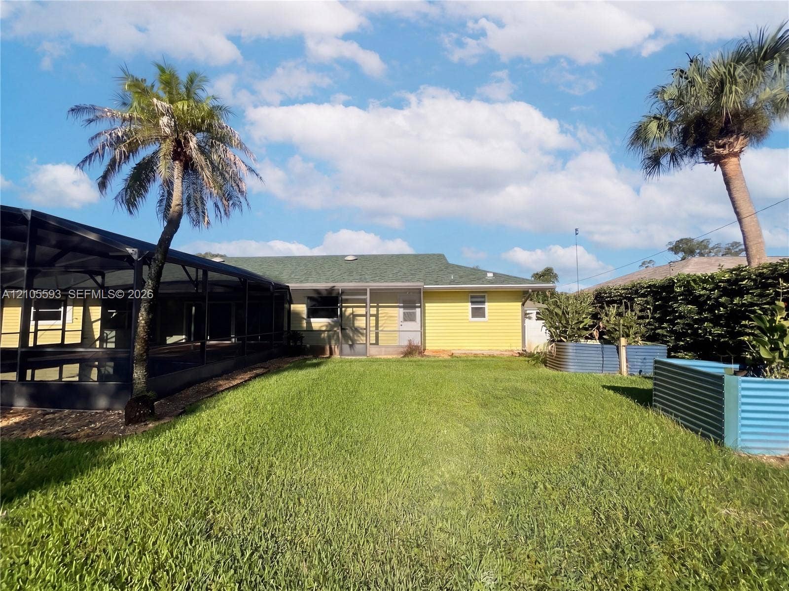 597 Grace Street, Sebastian, FL 32958 Backyard featuring a screened-in lanai, yellow horizontal siding, a green shingle roof, and corrugated metal garden beds