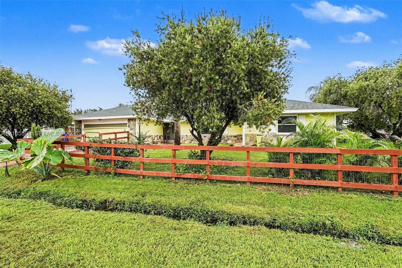 597 Grace Street, Sebastian, FL 32958 Single-story residence featuring stone masonry accents, a attached two-car garage, and a three-rail perimeter fence on a landscaped lot with mature trees