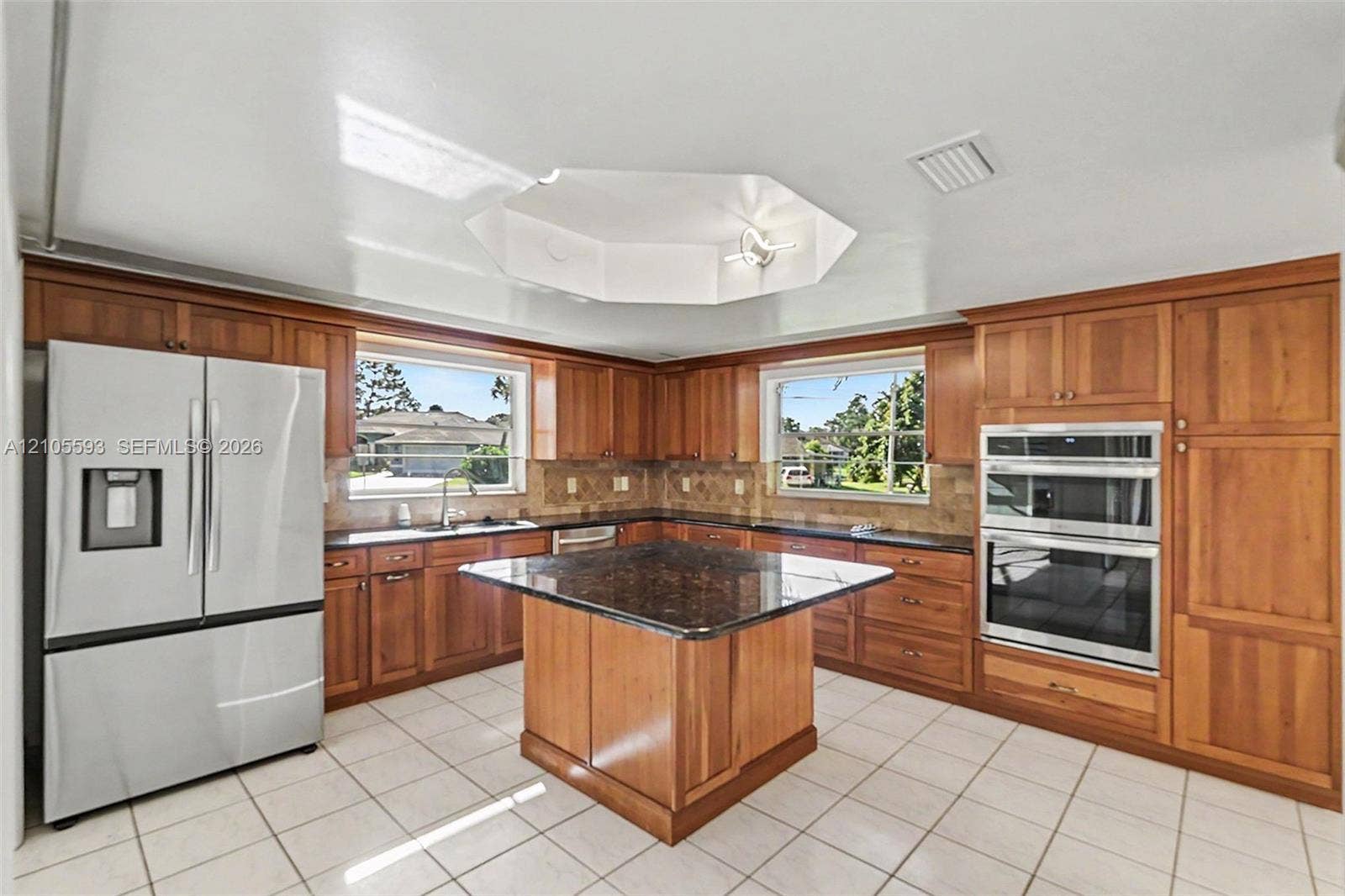 597 Grace Street, Sebastian, FL 32958 Kitchen featuring natural wood cabinetry, stone-surfaced central island, stainless steel double wall ovens, tile flooring, and a recessed hexagonal ceiling detail