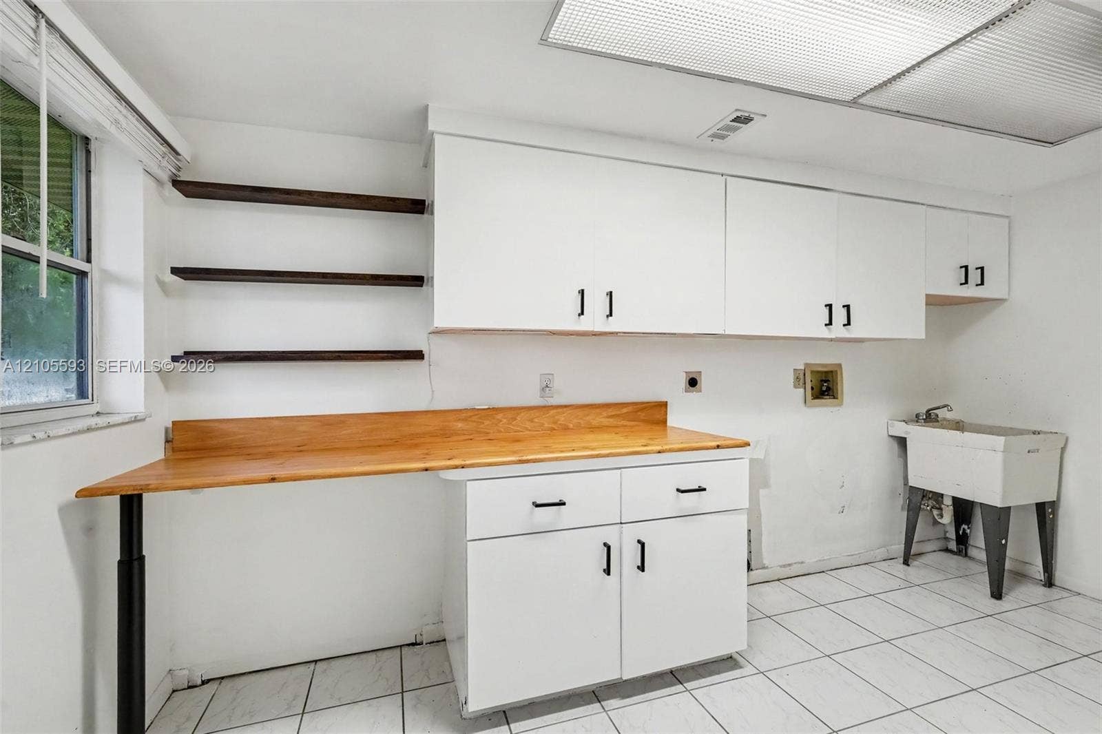 597 Grace Street, Sebastian, FL 32958 Work space featuring a wood-top counter, wall-mounted open shelving, white cabinetry, ceramic floor tiling, and a utility sink