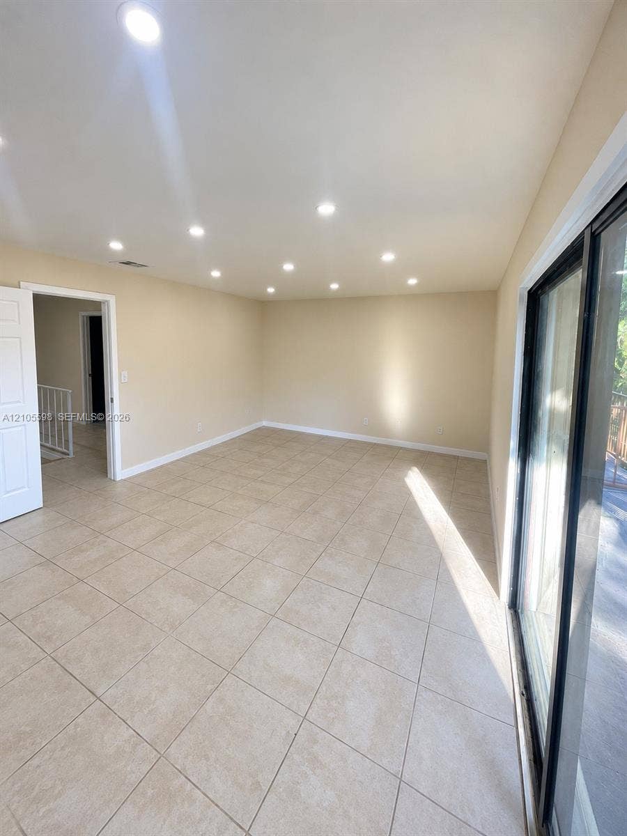 Recessed lighting, neutral wall tones, large format tile flooring, and a sliding glass door
