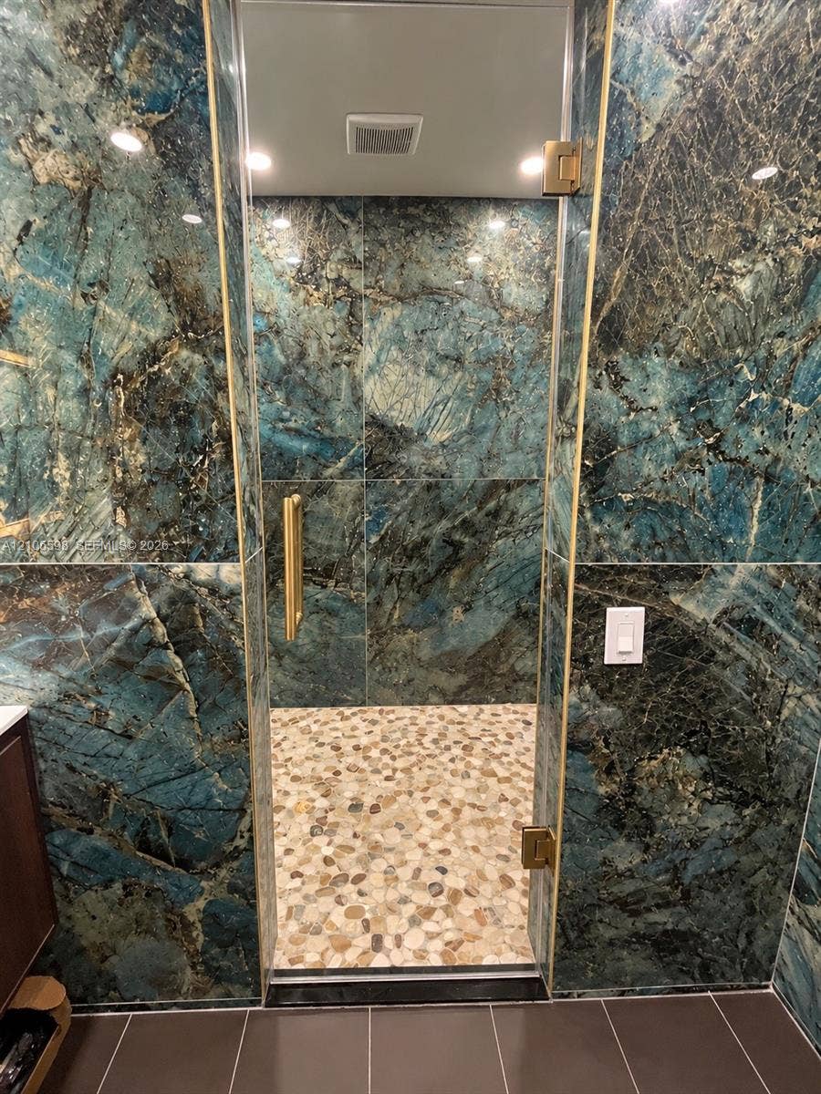 Walk-in shower featuring full-height natural stone walls, a natural pebble floor, and a frameless glass enclosure with brass hardware