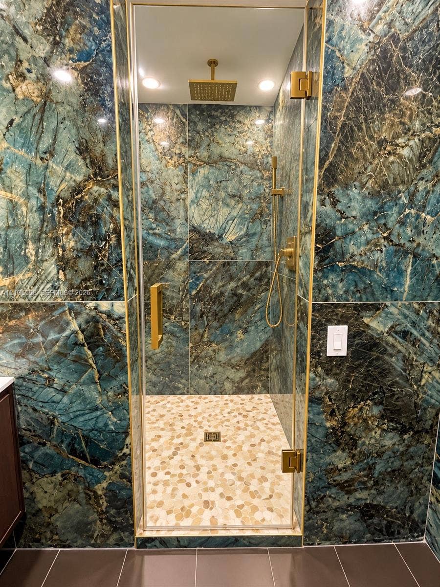 Walk-in shower featuring distinctively veined wall tile, a rain shower head, and gold-finish fixtures