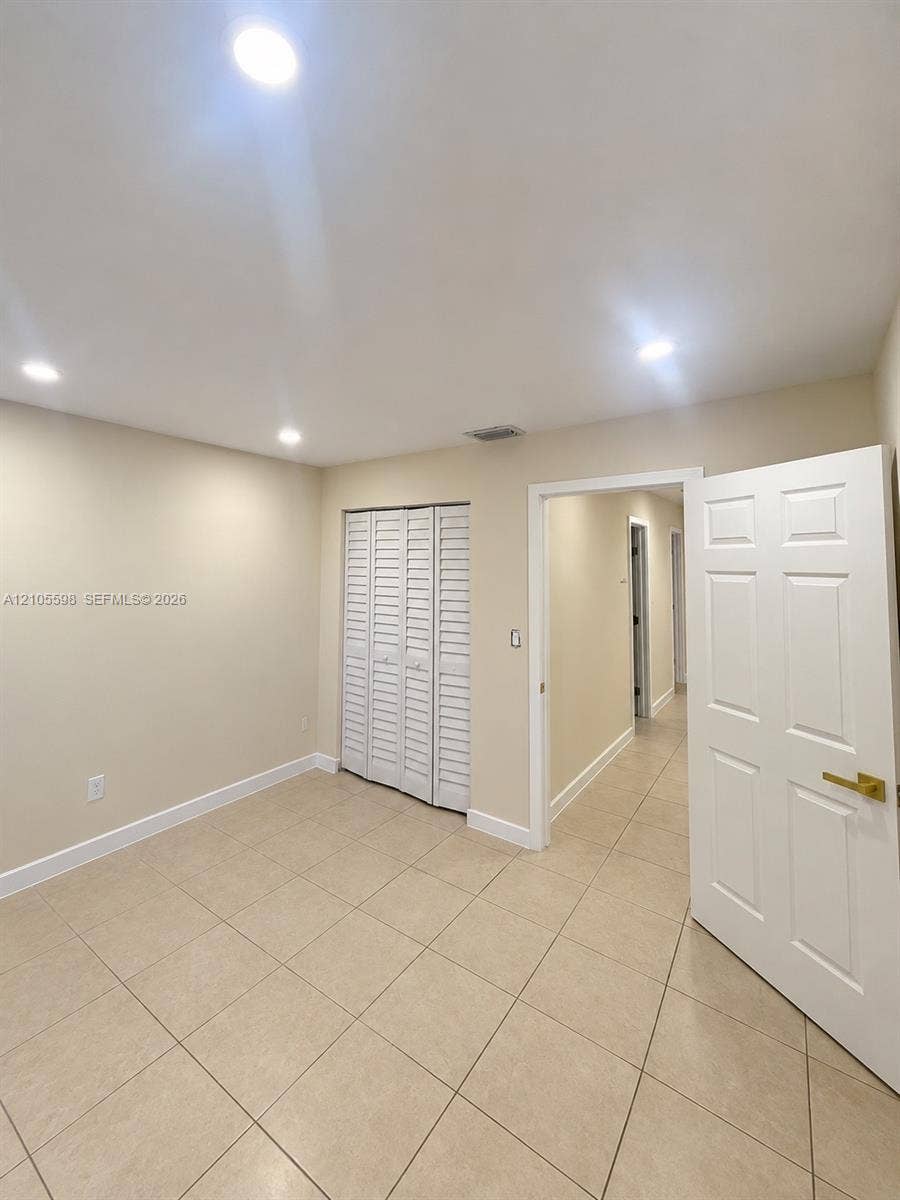Recessed ceiling lighting, neutral-toned walls, tile flooring, white bi-fold closet doors, and white paneled interior doors with brass hardware