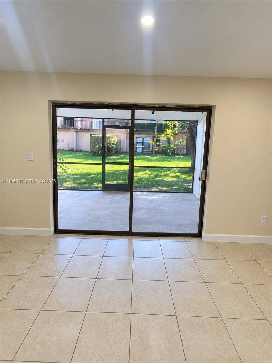 Recessed ceiling lighting, light-toned wall paint, tiled flooring, screened sliding glass door, and a paved patio