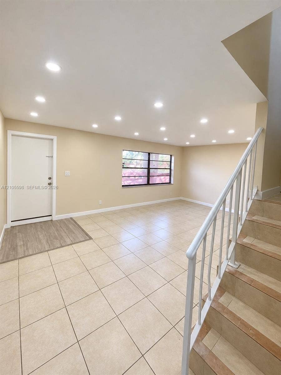 Recessed lighting, neutral wall tones, square tile flooring, window with horizontal blinds, and staircase with metal railing
