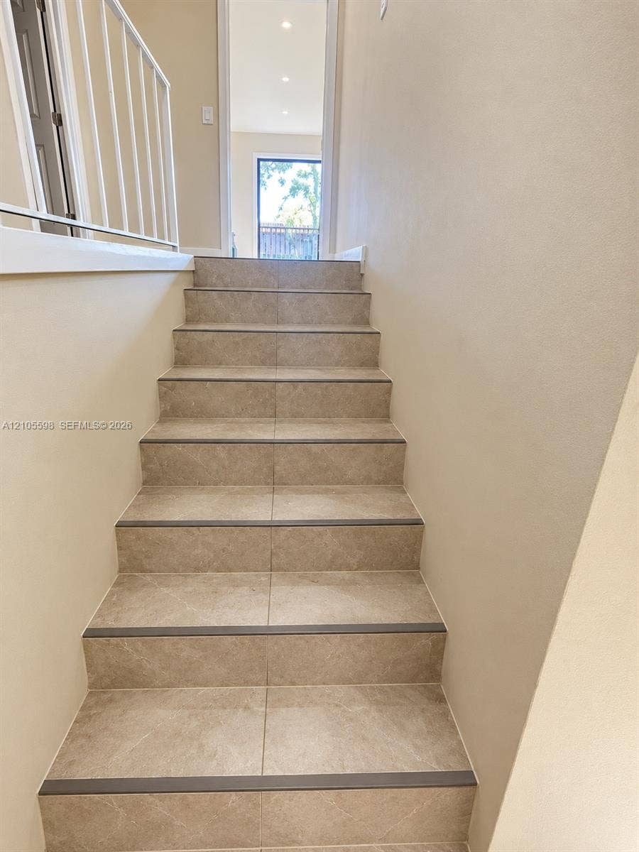 Tiled staircase with dark trim accents and a white metal railing