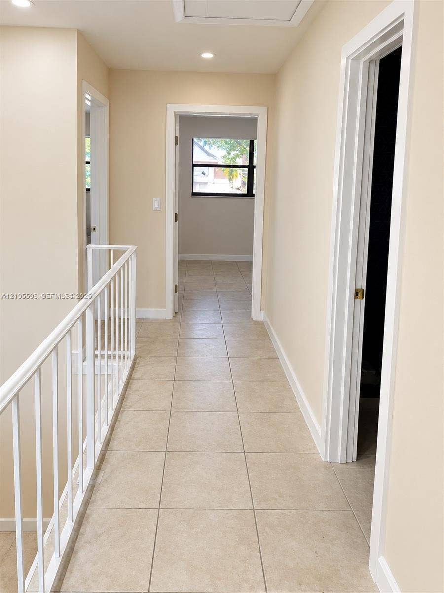 Hallway with neutral tone walls, recessed lighting, and square tile flooring