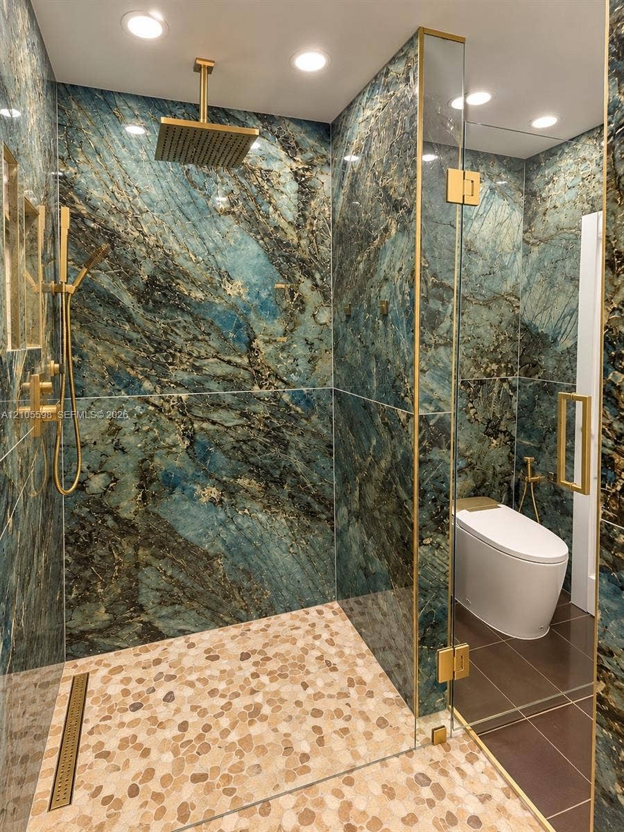 Walk-in shower with natural stone wall tiling, pebble-stone shower base, and gold-finish fixtures