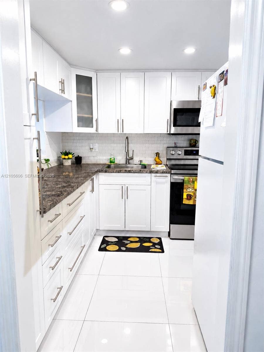 Contemporary kitchen featuring white cabinetry, a subway tile backsplash, dark countertops, recessed lighting, and stainless steel appliances