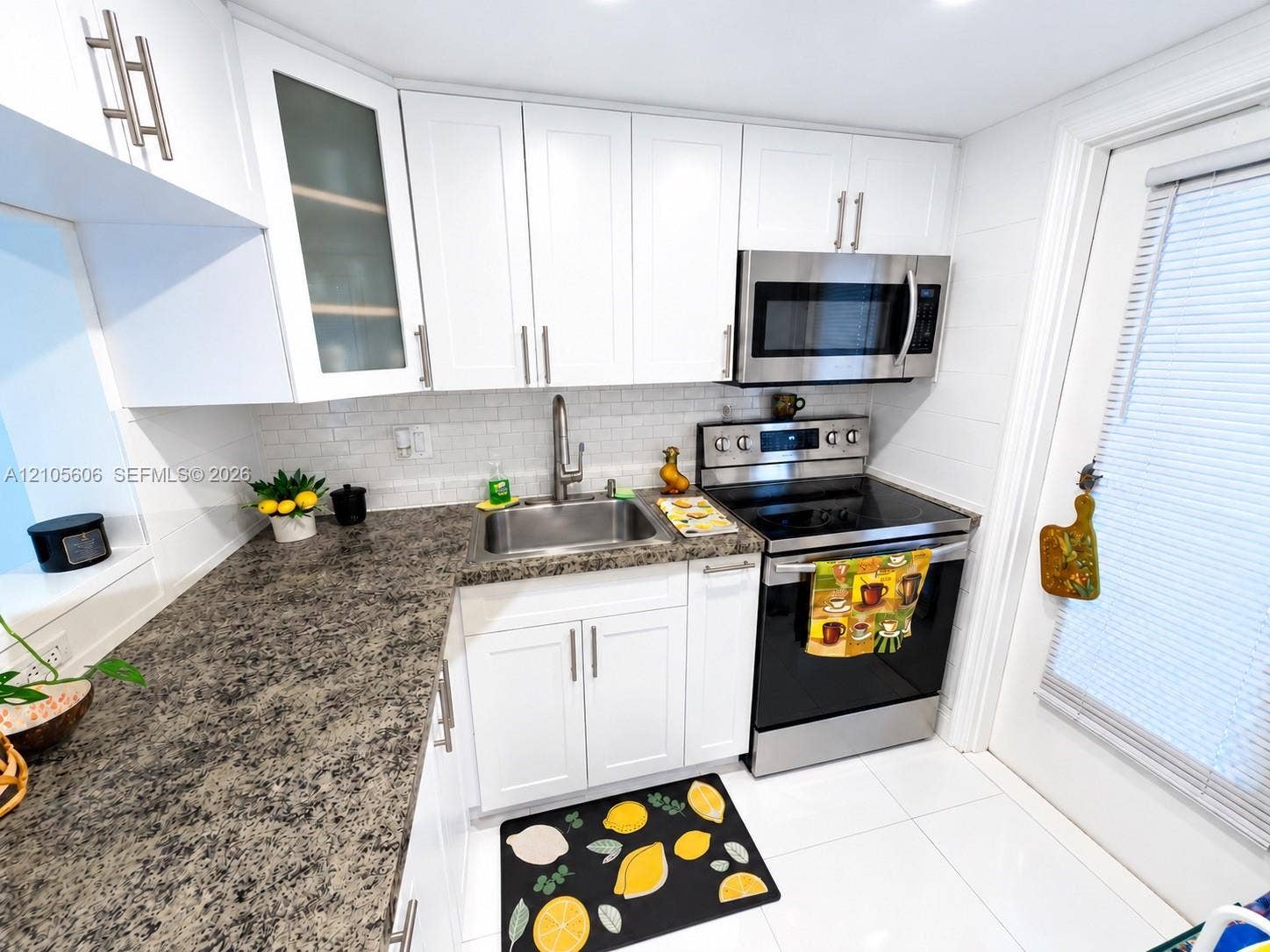 White shaker cabinetry, stainless steel appliances, granite-finish countertops, tile backsplash, and tile flooring