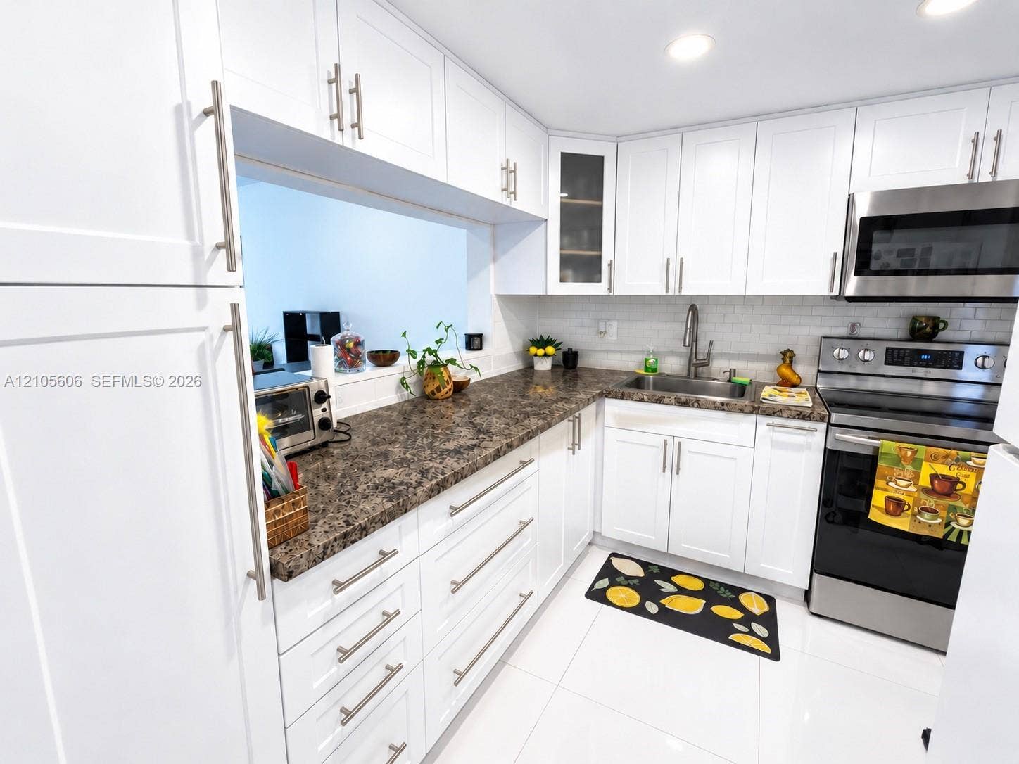 White shaker-style cabinetry with brushed nickel hardware, speckled countertops, stainless steel appliances, and white tile flooring