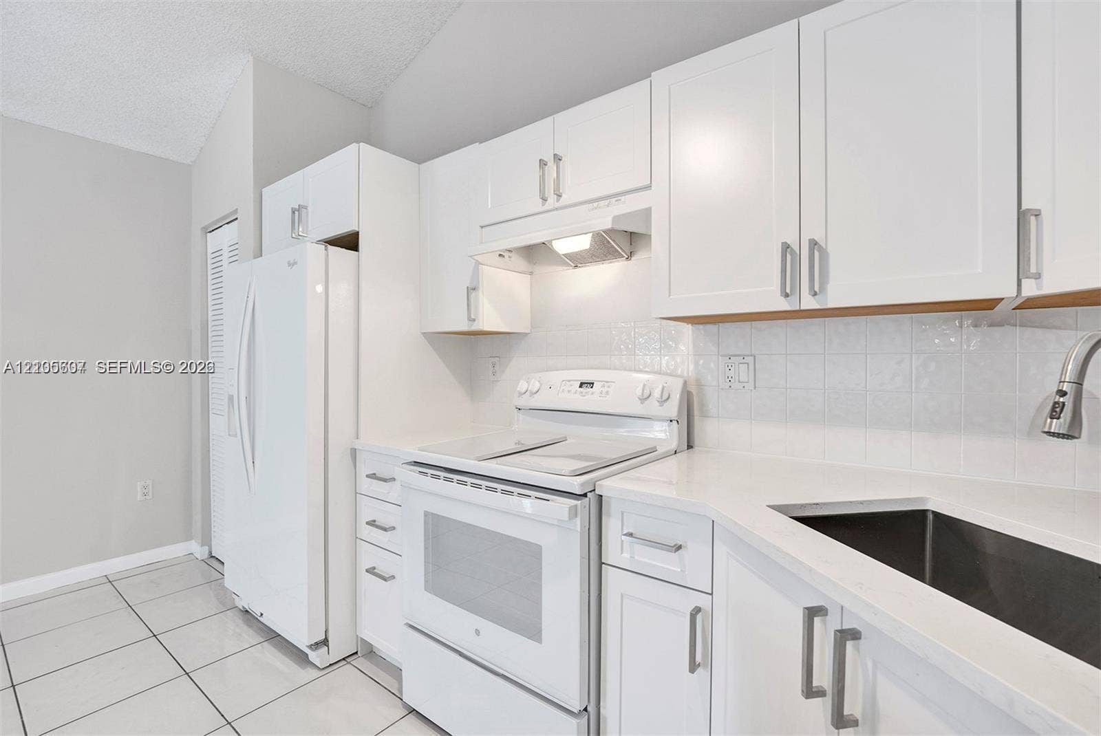 9892 Boca Gardens Parkway, #A, Boca Raton, FL 33496 White cabinetry with brushed nickel hardware, solid surface countertops, a tile backsplash, and a stainless steel sink with a gooseneck faucet