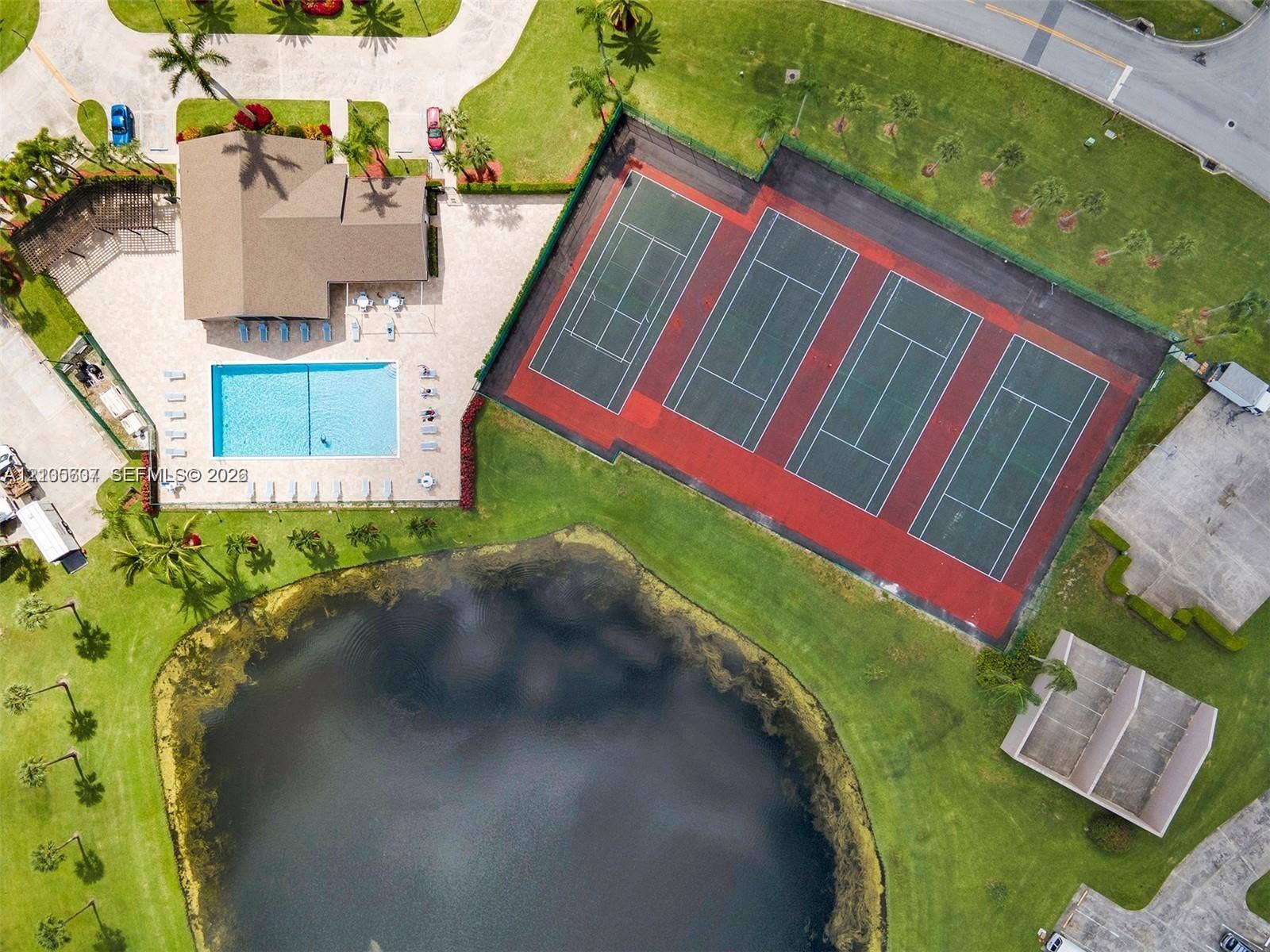 9892 Boca Gardens Parkway, #A, Boca Raton, FL 33496 Community building with a shingled roof, a rectangular swimming pool, multiple tennis courts, and a natural water feature