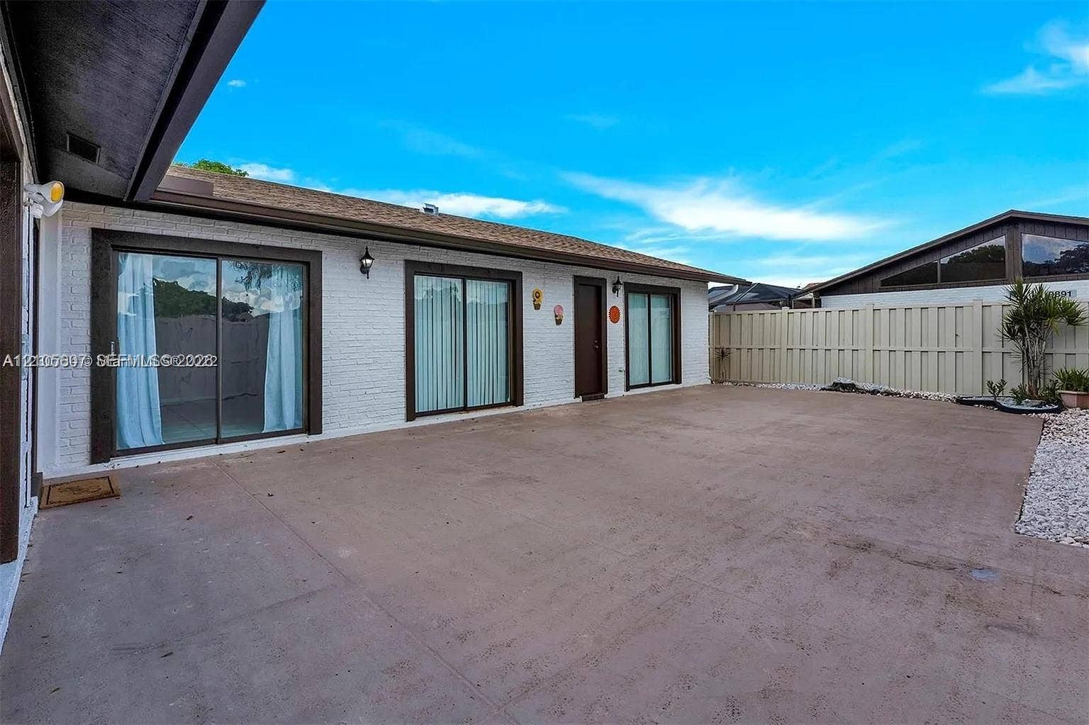 9892 Boca Gardens Parkway, #A, Boca Raton, FL 33496 Expansive concrete patio with white-painted brick exterior and dual sliding glass doors