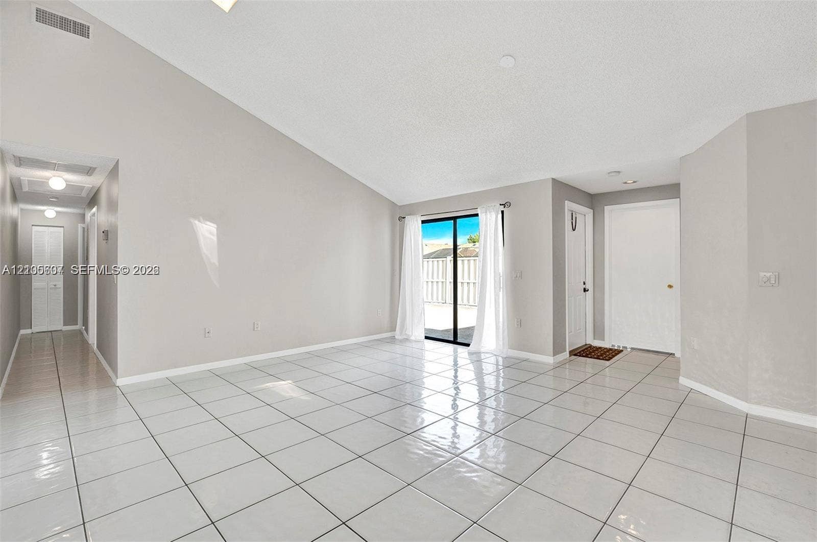 9892 Boca Gardens Parkway, #A, Boca Raton, FL 33496 Vaulted ceiling, white tile flooring, sliding glass door, recessed lighting, and a hallway with overhead lighting