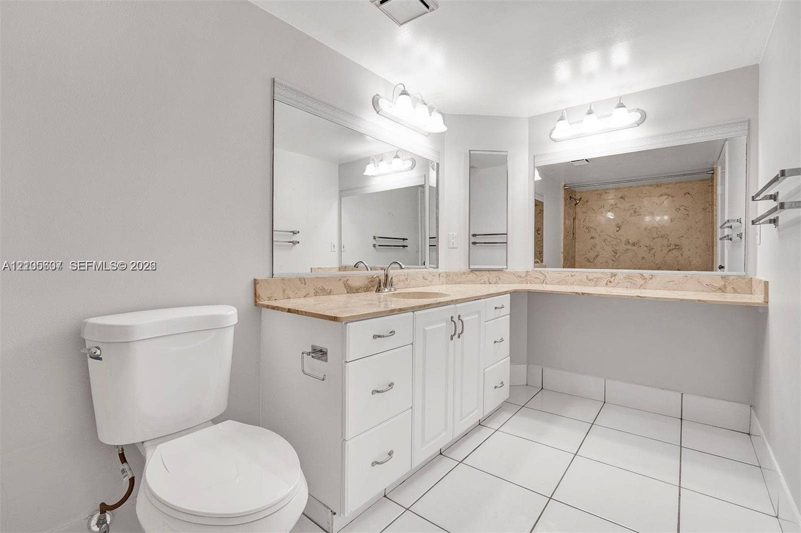 9892 Boca Gardens Parkway, #A, Boca Raton, FL 33496 White tile flooring, white vanity with integrated sink, stone countertop, mirrored wall, and wall-mounted light fixtures