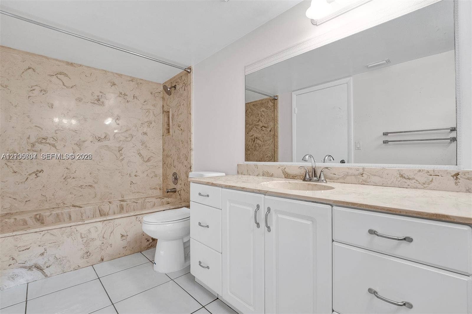 9892 Boca Gardens Parkway, #A, Boca Raton, FL 33496 Spa-inspired bathroom featuring a marble-look tile surround with integrated shower enclosure, white vanity cabinetry with brushed nickel hardware, stone-finish countertop, large framed mirror, and ceramic tile flooring