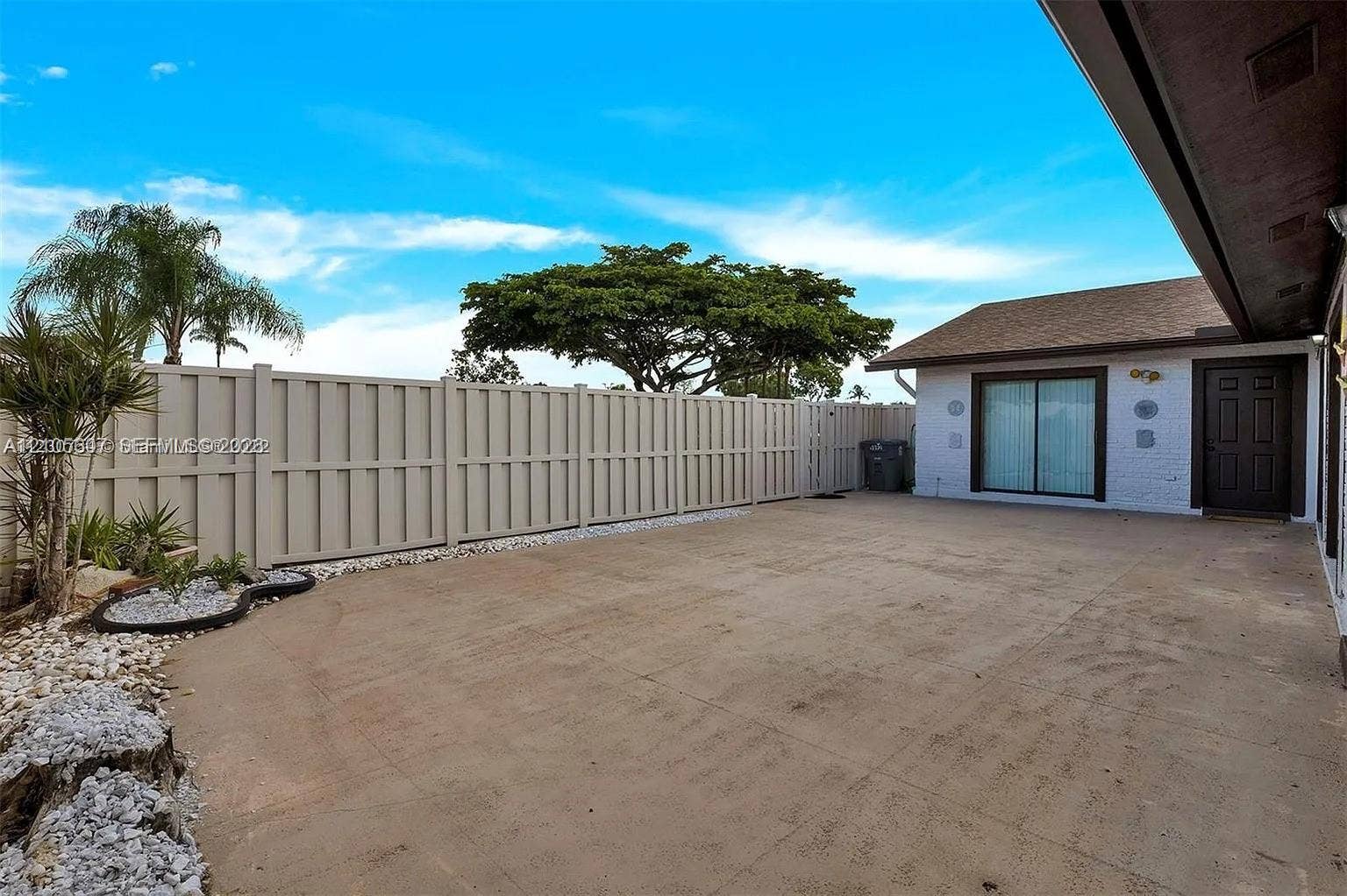 9892 Boca Gardens Parkway, #A, Boca Raton, FL 33496 Paved outdoor area with privacy fencing, mature landscaping, and sliding glass door access