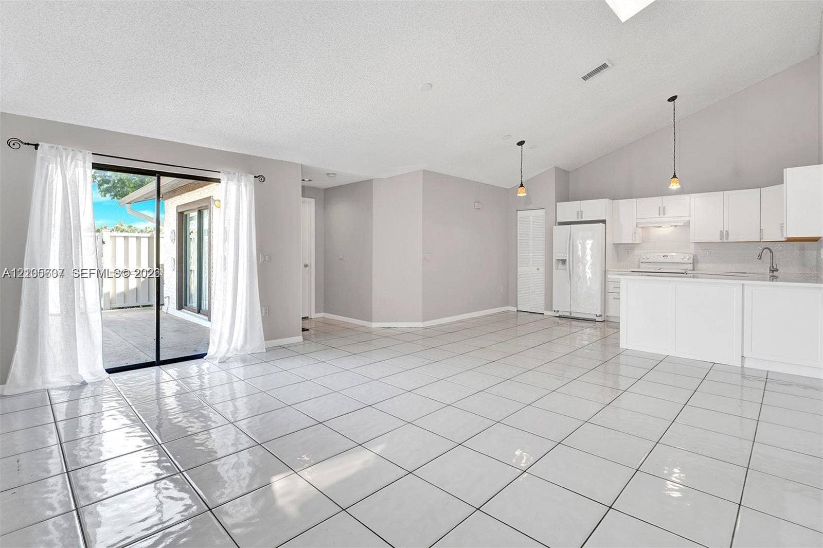 9892 Boca Gardens Parkway, #A, Boca Raton, FL 33496 Vaulted ceiling with a skylight, white tile flooring, white kitchen cabinetry, and sliding glass doors