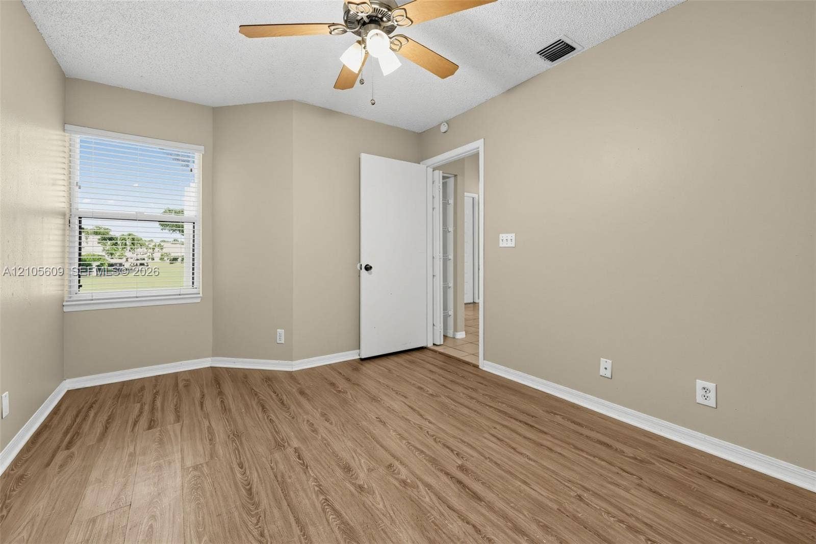 Neutral-toned interior space featuring wood-finish flooring, a multi-pane window, and a ceiling-mounted light fixture with a central fan