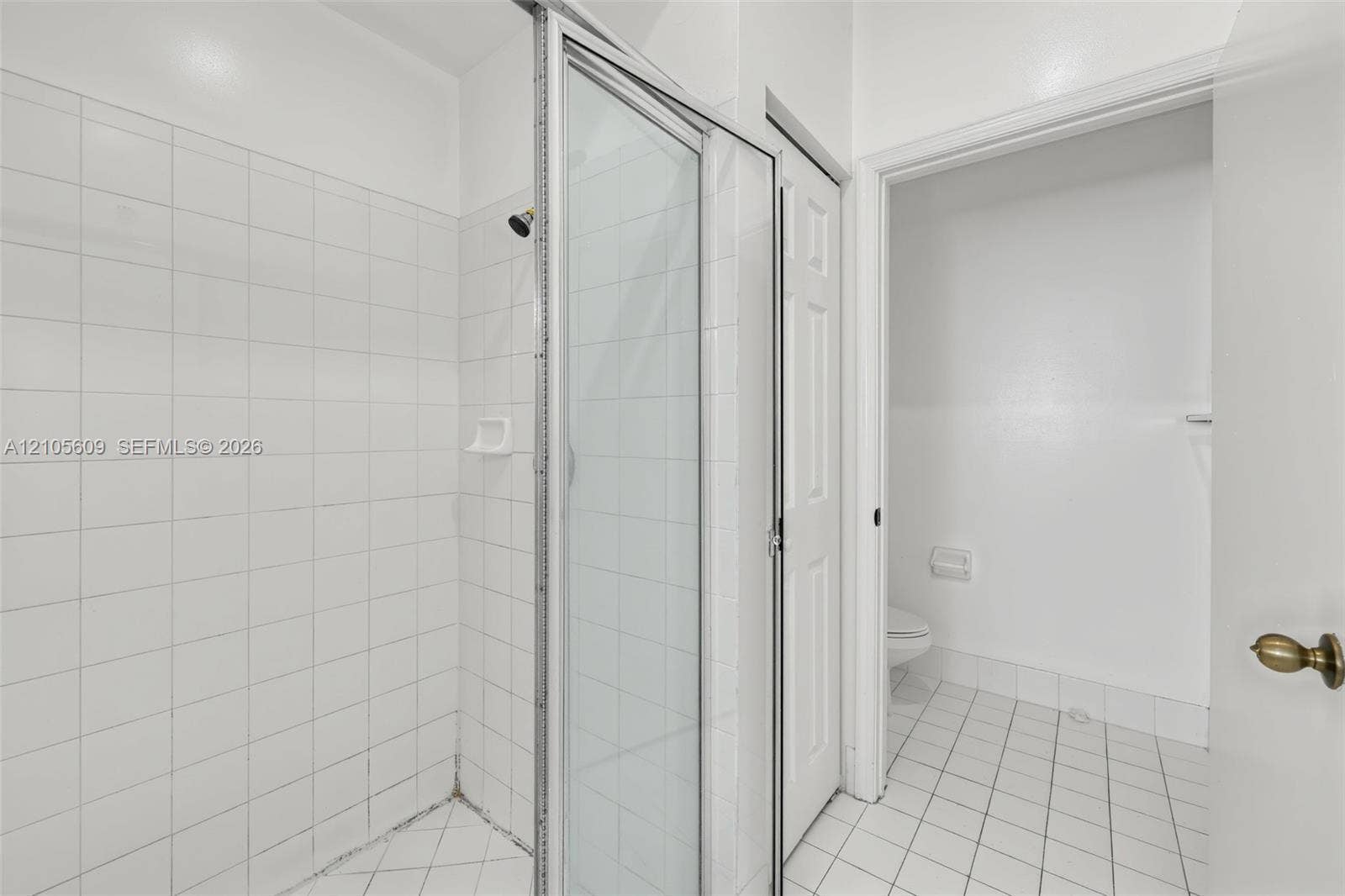 Shower stall with a glass door, white wall tiling, and white floor tiling