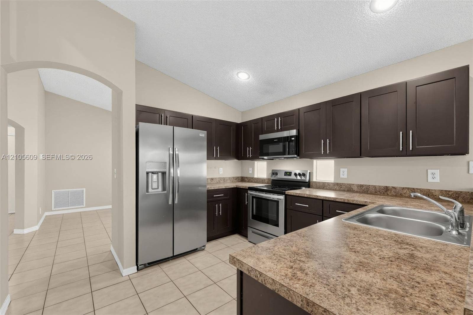 Kitchen featuring dark-toned cabinetry, stainless steel appliances, expansive stone-finish countertops, recessed lighting, and tile flooring