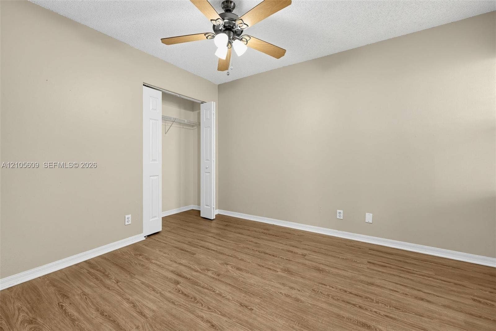 Room featuring wood-finish flooring, neutral wall paint, a ceiling fan with integrated lighting, and a closet with bifold doors