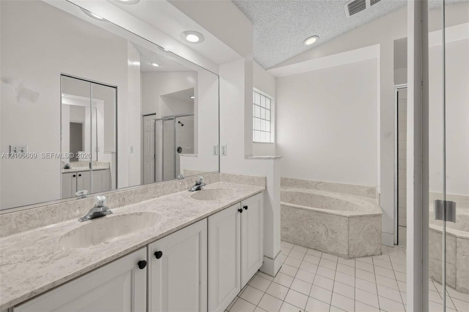 Dual-sink vanity with stone-finish countertop, full-width mirror, recessed lighting, and separate built-in soaking tub with surround