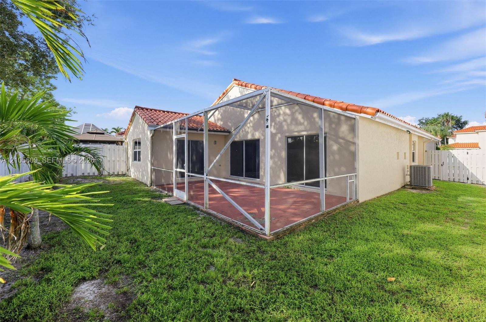 Rear exterior featuring a screened-in lanai with tile flooring, stucco siding, and a red tile roof, complemented by a fenced-in lawn