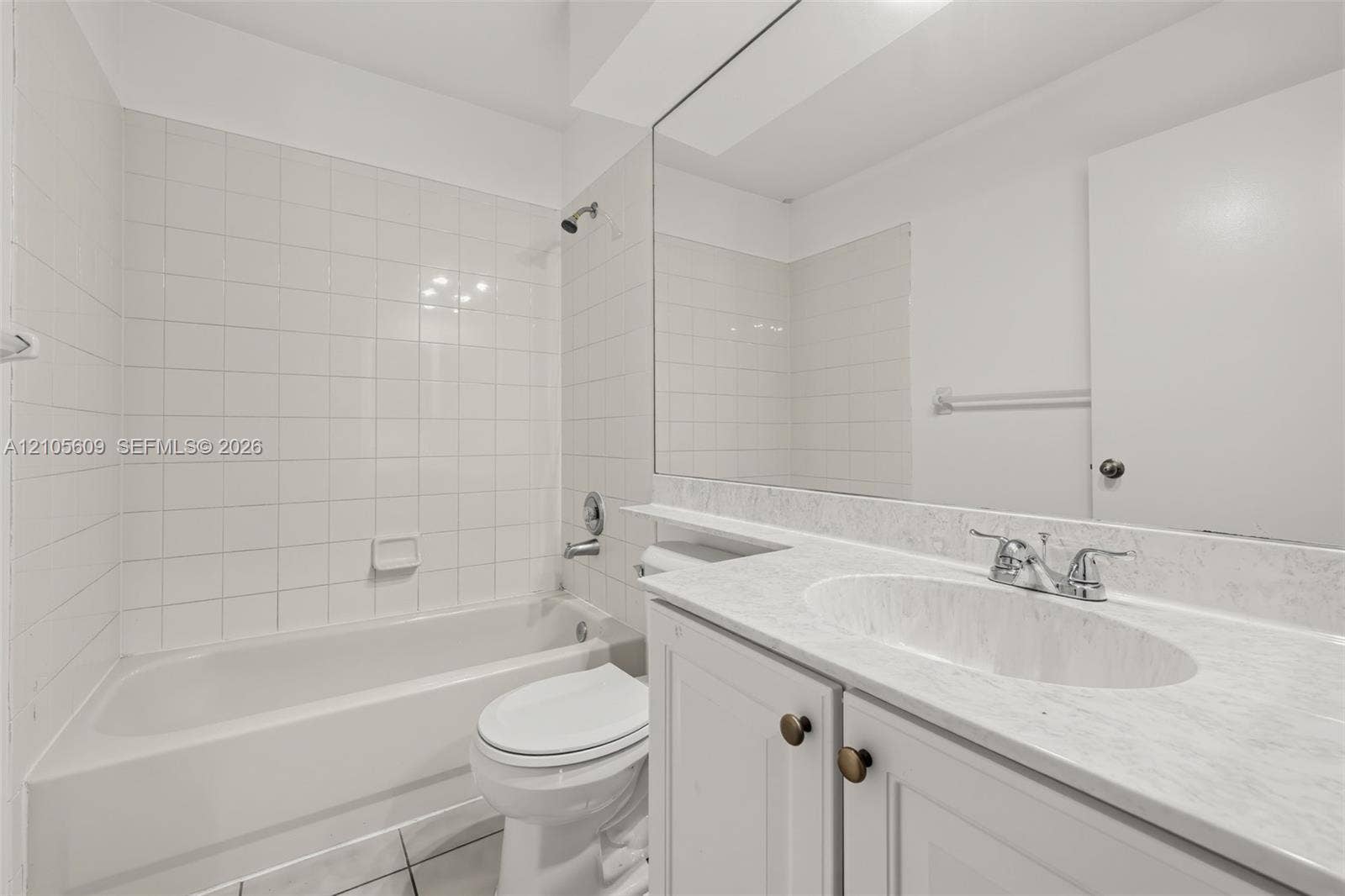 Bathroom featuring a white bathtub with a tile surround, vanity with a light-toned stone-patterned countertop, integrated oval sink, and a full-width wall mirror