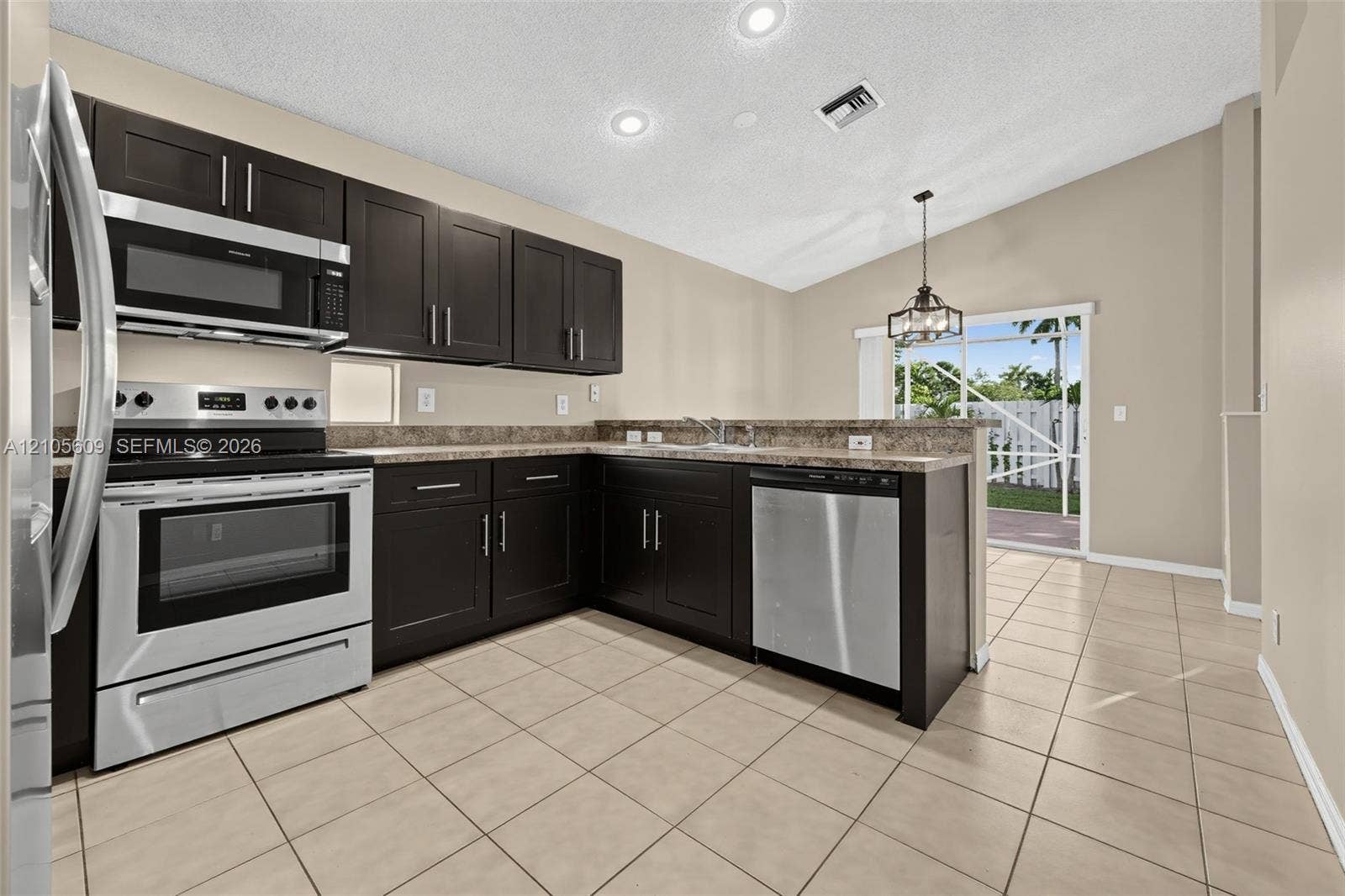 Kitchen featuring dark wood-finish cabinetry, stone-finish countertops, stainless steel appliances, tile flooring, and vaulted ceilings