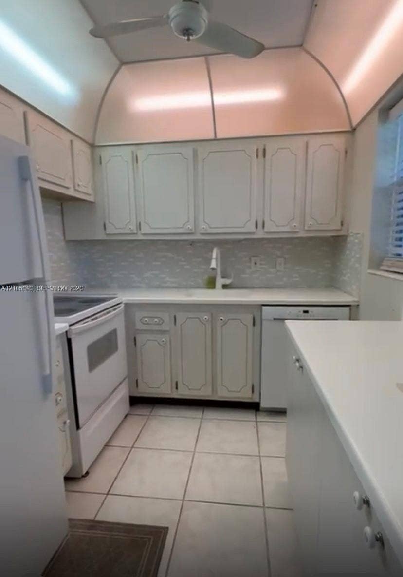 573 Durham U, #573, Deerfield Beach, FL 33442 Kitchen featuring white cabinetry, solid-surface countertops, tile backsplash, white appliances, and vaulted ceiling with integrated lighting