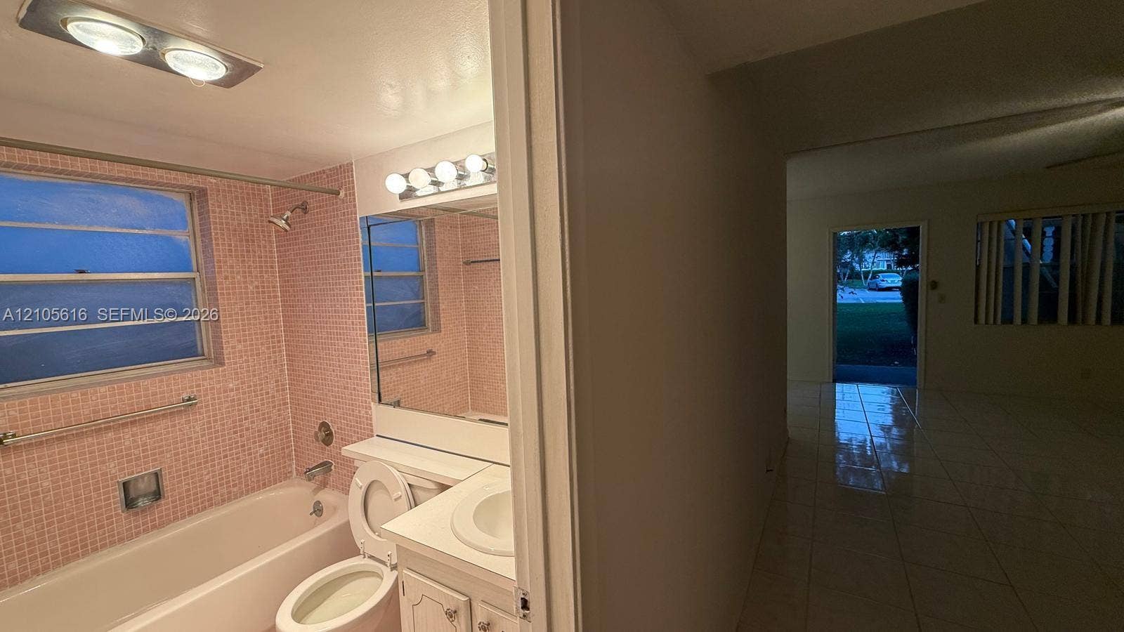 573 Durham U, #573, Deerfield Beach, FL 33442 Bathroom featuring a built-in vanity with an integrated basin, a large wall-mounted mirror with multi-bulb light fixture, a shower-tub combination with mosaic tile wall surround, and polished tile flooring extending into the hallway