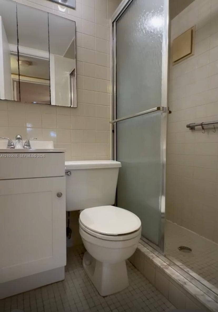 573 Durham U, #573, Deerfield Beach, FL 33442 Bathroom featuring a white vanity cabinet, integrated sink with chrome faucet, wall-mounted mirrored medicine cabinet, and a walk-in shower with a sliding glass door and tiled surround