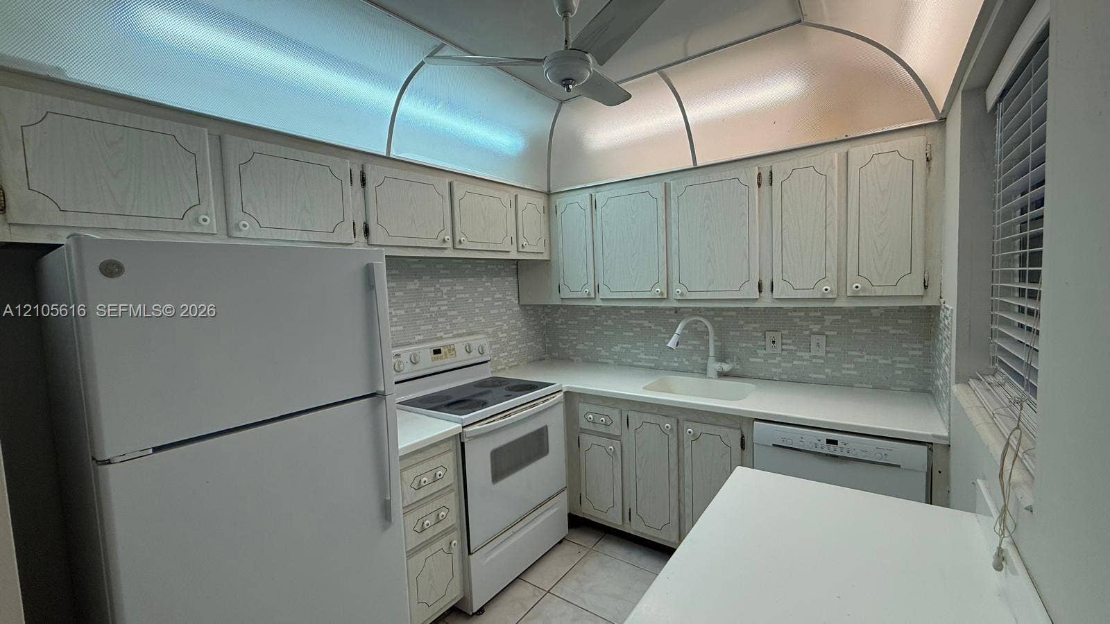573 Durham U, #573, Deerfield Beach, FL 33442 Kitchen featuring light-toned cabinetry with decorative millwork, solid-surface countertops, a textured tile backsplash, integrated cove lighting, and a ceiling-mounted fan