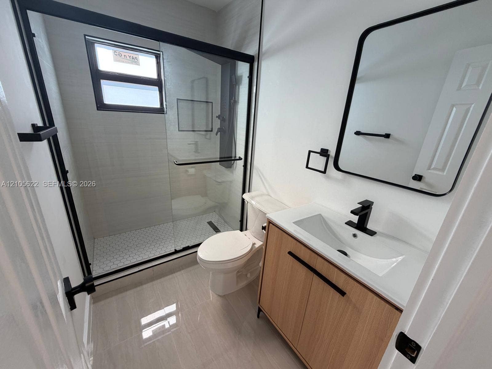 9728 Little River Drive, Miami, FL 33147 Bathroom featuring a wood-finish vanity with a white rectangular sink, matte black hardware, a walk-in shower with a glass enclosure, and hexagonal tile flooring