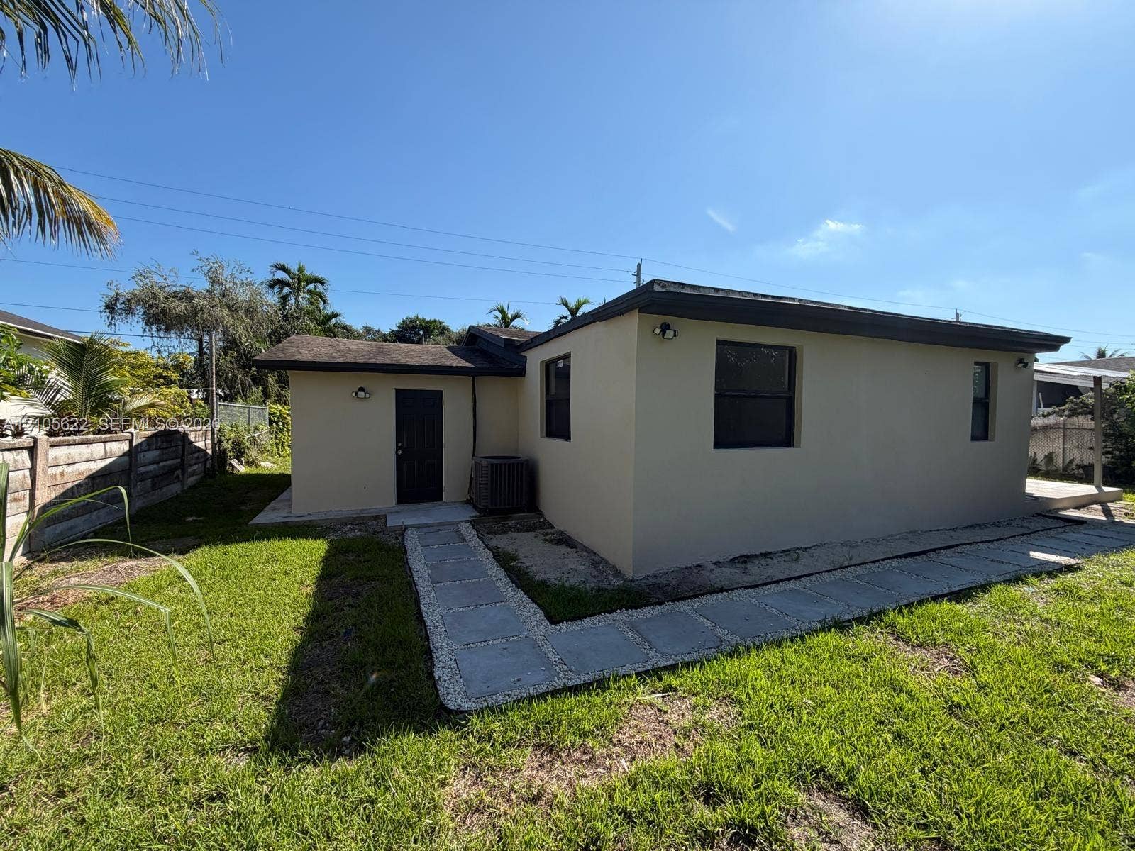 9728 Little River Drive, Miami, FL 33147 Stucco exterior featuring dark-framed windows, a dedicated entry point, and concrete paver pathway set within a grass lawn