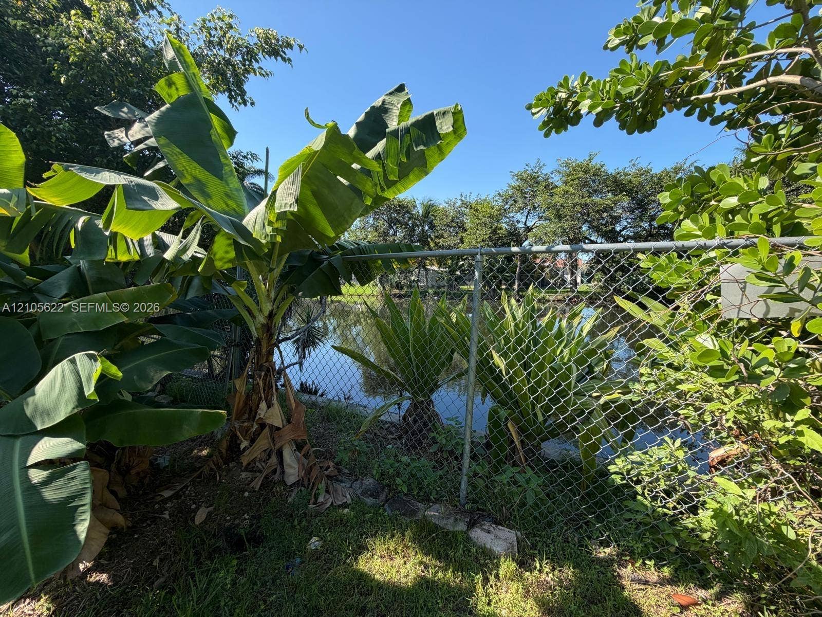 9728 Little River Drive, Miami, FL 33147 Waterfront lot featuring mature tropical landscaping and chain-link fencing