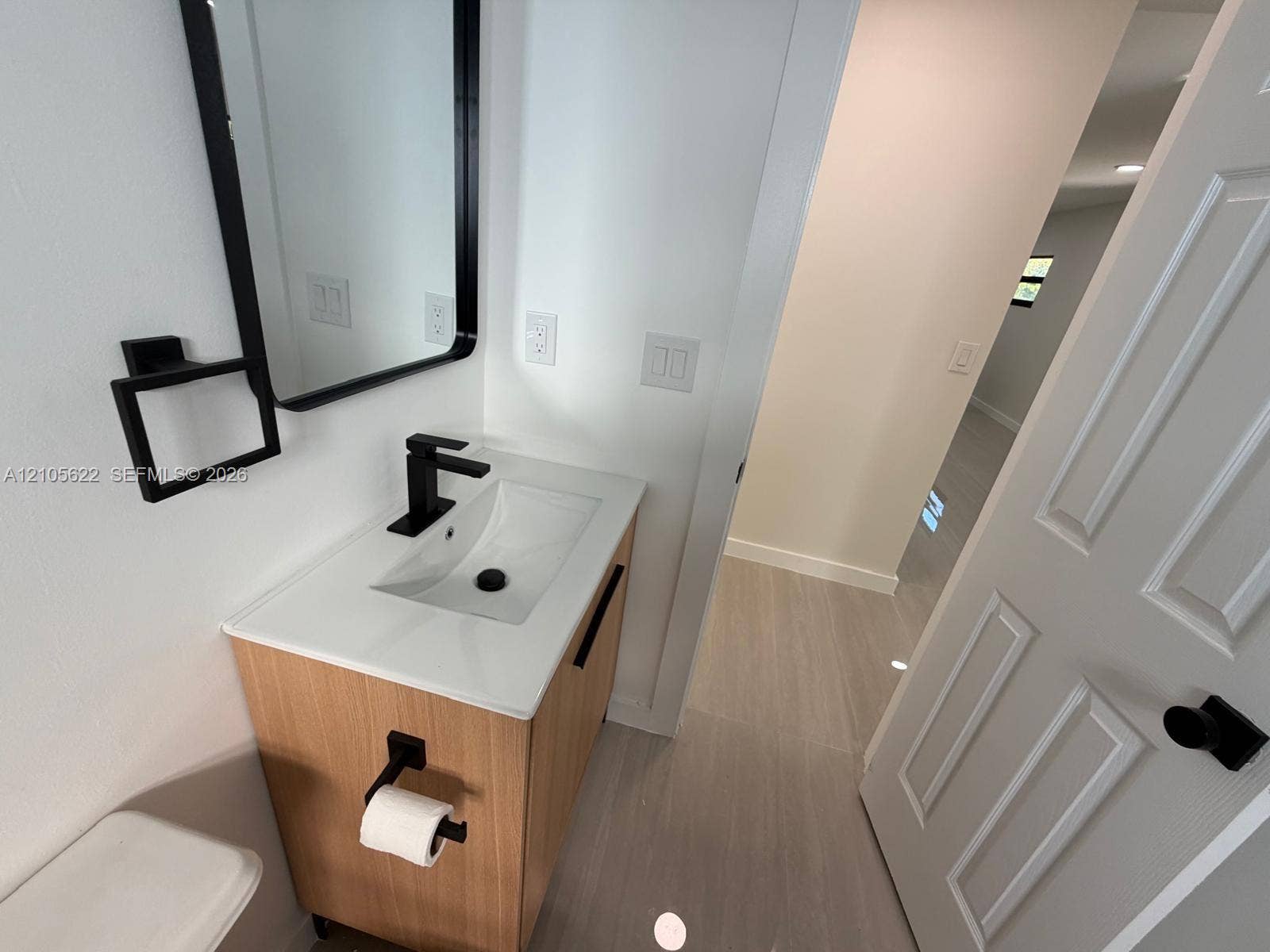 9728 Little River Drive, Miami, FL 33147 Wood-finish vanity with a white integrated sink, matte black faucet, rectangular mirror with a black frame, and coordinated matte black hardware