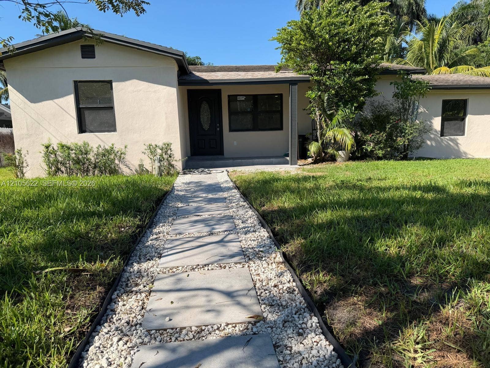 9728 Little River Drive, Miami, FL 33147 Stucco exterior residence featuring a paved stone walkway with decorative gravel borders, an oval-paneled front entry door, and a covered porch area