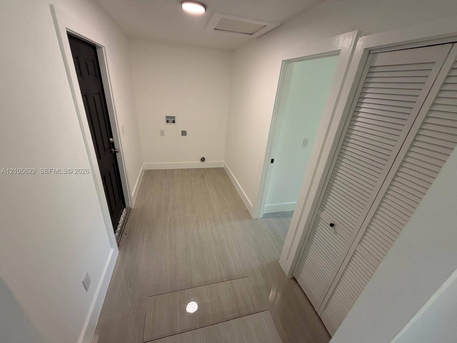 9728 Little River Drive, Miami, FL 33147 Utility space featuring wood-finish flooring, a dark-toned door with paneled detailing, white louvered-style closet doors, and flush-mount ceiling lighting