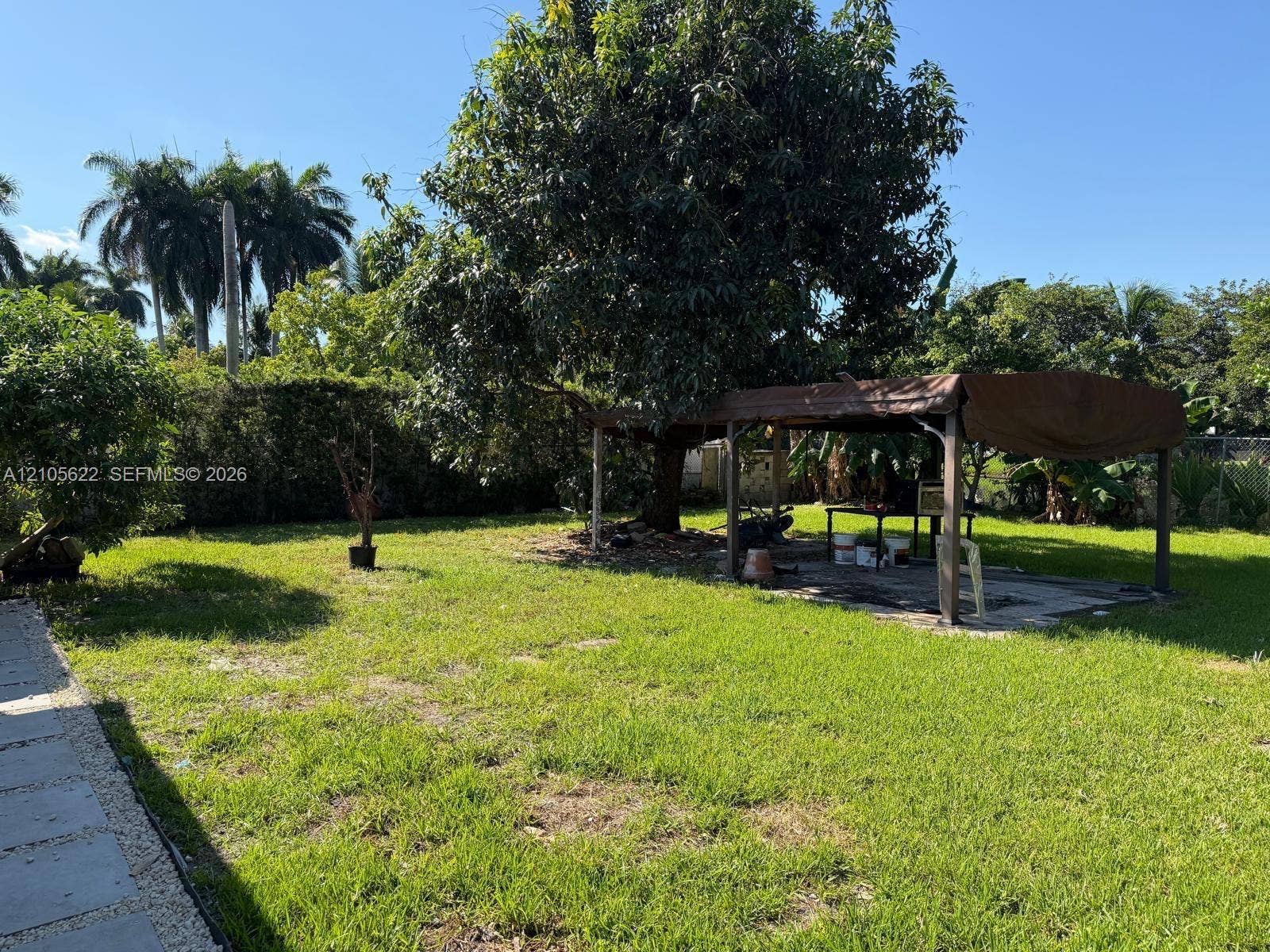 9728 Little River Drive, Miami, FL 33147 Expansive backyard featuring a sprawling lawn, mature trees, a paved stone walkway, and an open-air metal structure
