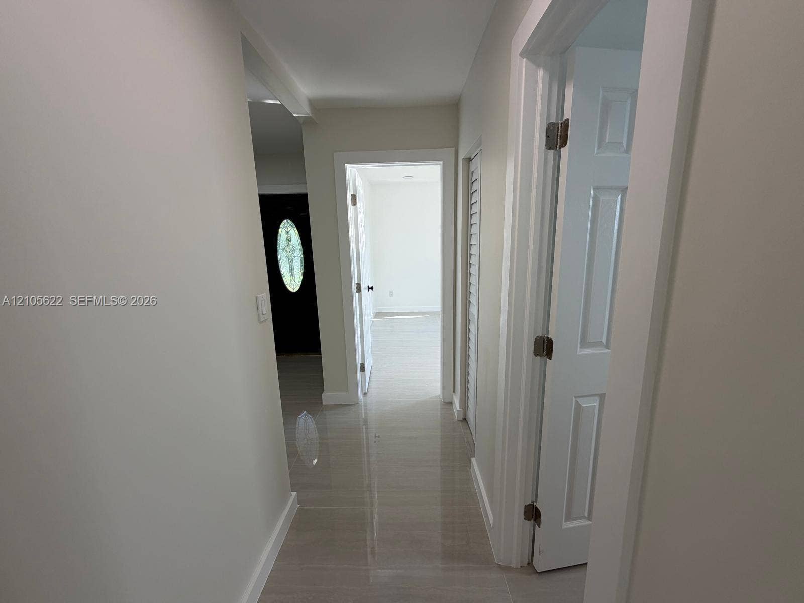 9728 Little River Drive, Miami, FL 33147 Interior hallway featuring large-format tile flooring, crisp white walls, white six-panel doors, and a louvered closet door
