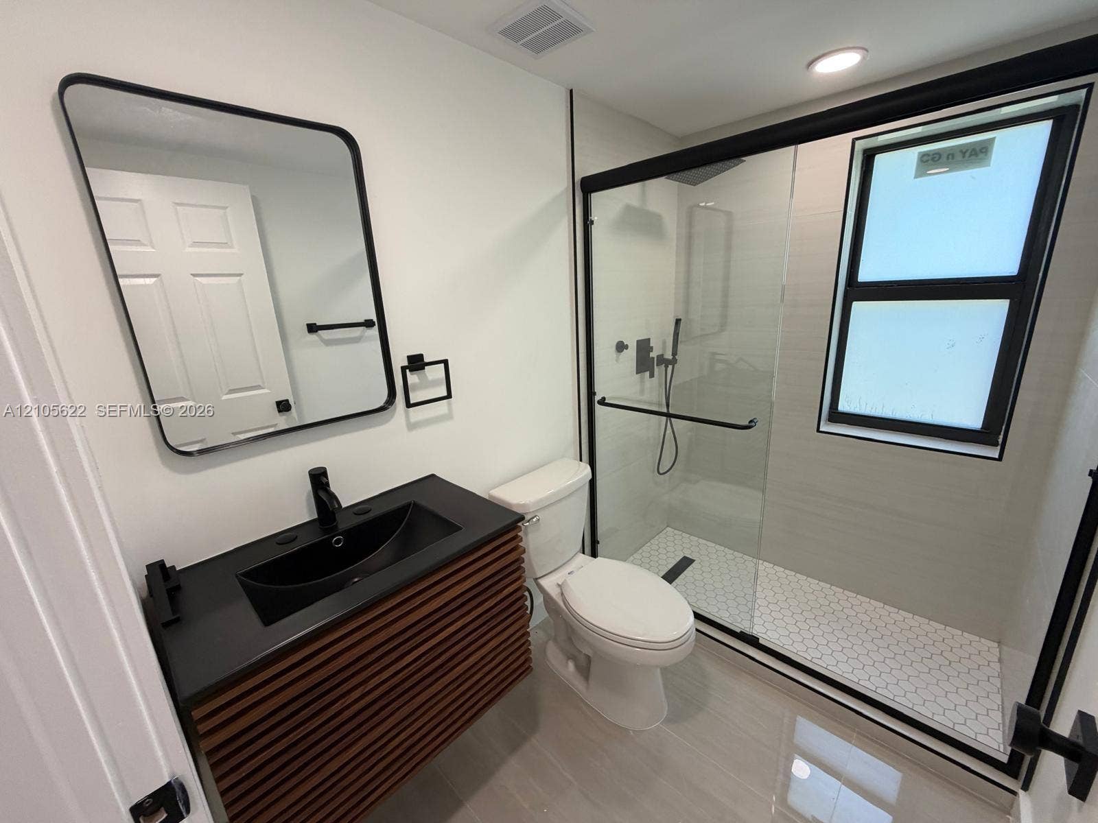 9728 Little River Drive, Miami, FL 33147 Floating vanity with slatted wood-finish base, rectangular basin, matte black fixtures, and walk-in shower with glass enclosure and hexagonal tile flooring
