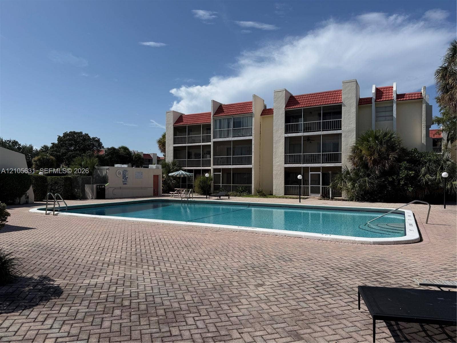 610 NW 13th Street, #0140, Boca Raton, FL 33486 In-ground swimming pool with handrails, surrounded by a herringbone-patterned paver deck and multi-story building exterior featuring red tile roofing